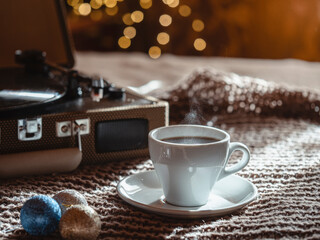 White cup of coffee with smoke on the background of Christmas lights and vinyl. Cozy Christmas atmosphere