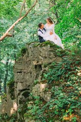 the newlyweds sit on a rock and hug. rock in the forest among th