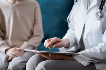 Doctor woman using touchpad while sitting with kid patient on blue sofa. Medicine concept