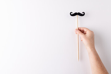 Hand holding black false moustache on stick, on white background with copy space