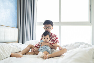 Brother and baby sister is playing on the white bed in the bedroom.The selective focus and space for copy and text.