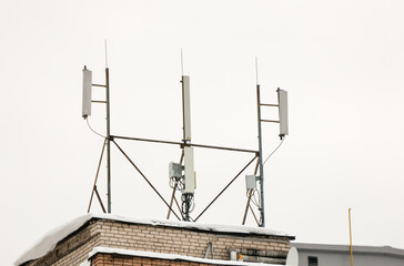 Several cellular antennas on the roof of the house provide communication. Snow lies on the milestone, against the background of a gray sky. Cloudy, cold winter day, soft light.