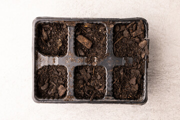 Overhead view of seedling tray filled with dark soil and bark pieces