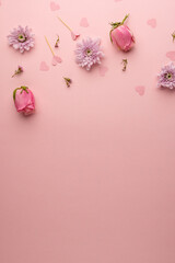 Vertical of pink flowerheads and heart confetti, on pink background with copy space