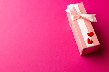 Pale pink gift box tied with white ribbon and red hearts, on pink background with copy space