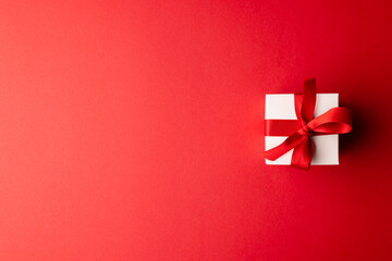 Overhead of white gift box tied with red ribbon, on red background with copy space