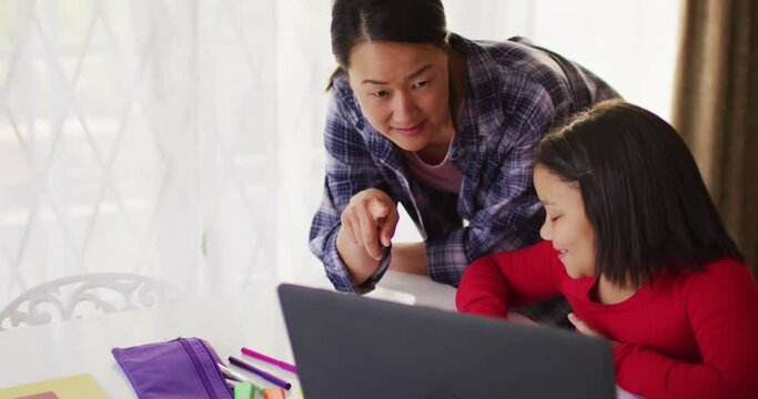 Video of happy asian mother and daughter doing homework together