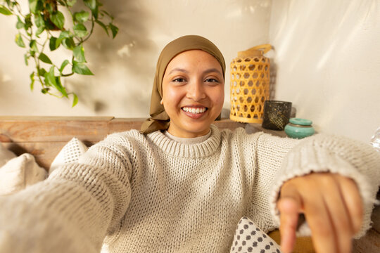 Happy biracial woman wearing hijab, having a video call - Powered by Adobe
