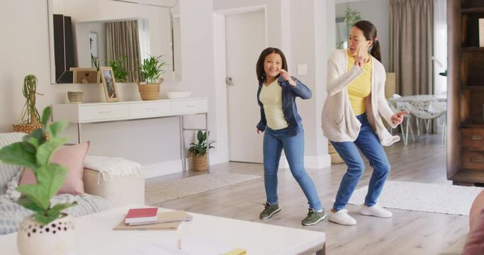 Video of happy asian mother and daughter dancing in living room