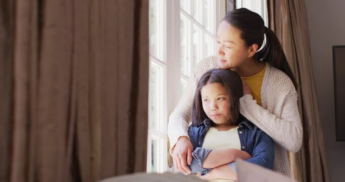 Video of thoughtful asian mother and daughter looking outside window