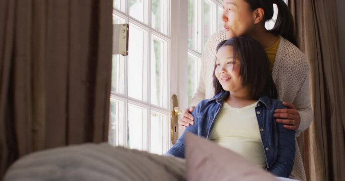 Video of thoughtful asian mother and daughter looking outside window