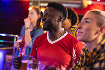 Diverse group of excited male and female friends watching sports game showing at a bar