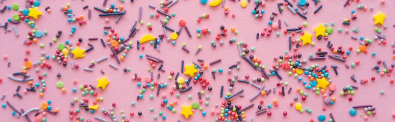 Top view of different sprinkles on pink background, banner.