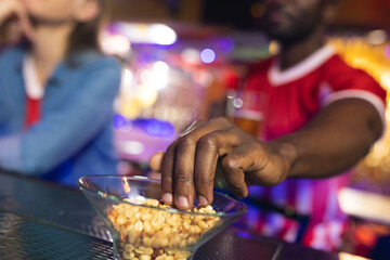 Two diverse male and female friends at the bar, man grabbing peanuts from bowl, selective focus