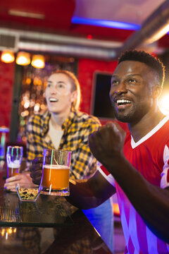 Vertical of diverse, excited male and female friend reacting to sports game showing at a bar