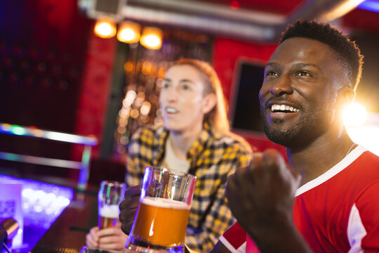 Diverse, Excited Male And Female Friend Reacting To Sports Game Showing At A Bar