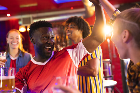 Diverse group of excited male and female friends watching sports game at a bar celebrating