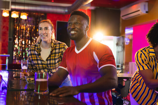 Diverse, excited male and female friend watching sports game showing at a bar