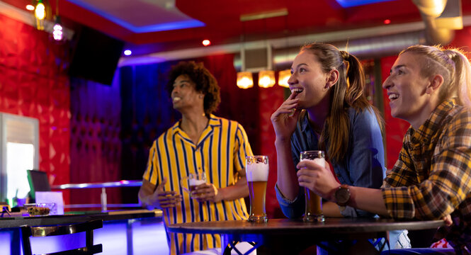 Three diverse excited male and female friends watching sports game showing at a bar