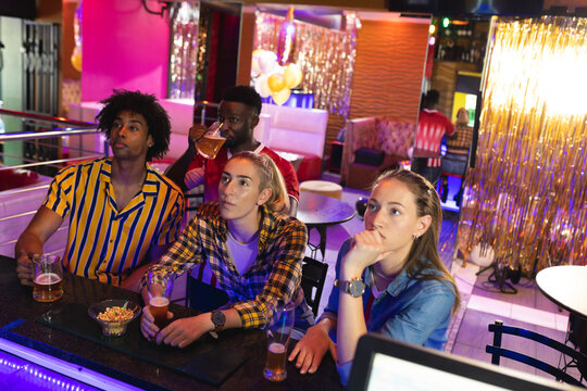 Four diverse, tense male and female friends watching sports game showing at a bar