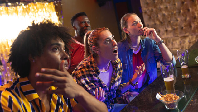 Four diverse, tense male and female friends watching sports game showing at a bar