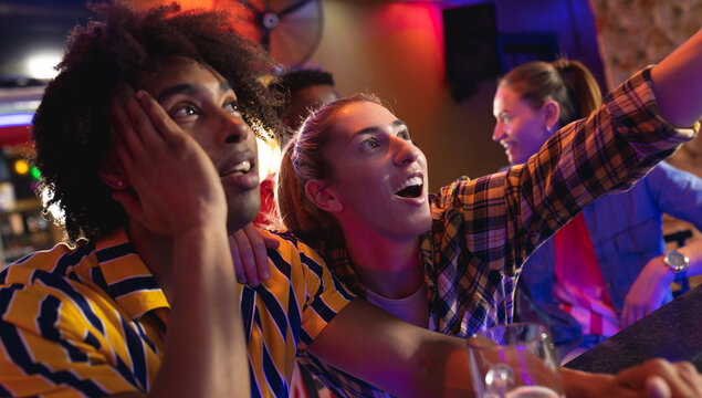Diverse group of excited male and female friends watching sports game showing at a bar