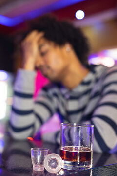 Vertical of drunk african american man holding head at bar, glasses in foreground, selective focus
