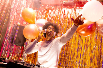 Smiling african american dj in headphones playing music at a nightclub and pointing