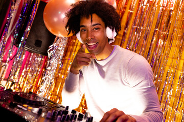 Portrait of smiling african american dj in headphones playing music at a nightclub pointing