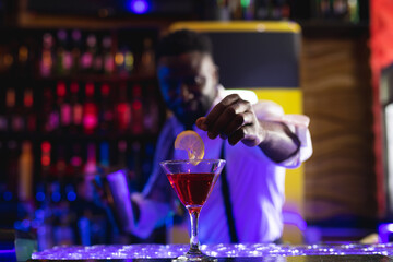 Smiling african american barman preparing pink cocktail at a bar