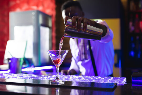 African american barman pouring pink cocktail at the bar of a nightclub
