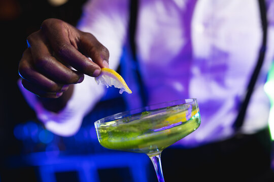Midsection of african american barman preparing green cocktail at a bar
