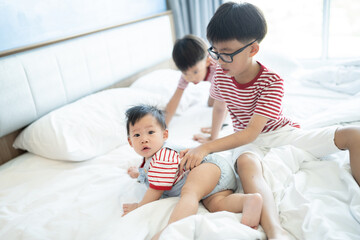 Fototapeta premium Brothers and baby sister is playing on the white bed in the bedroom.The selective focus and space for copy and text.