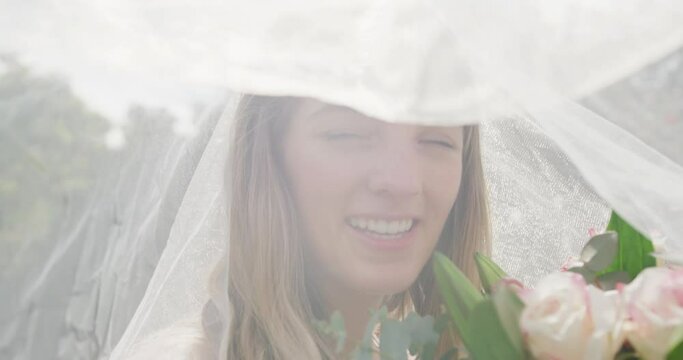 Portrait of happy caucasian woman with veil on sunny day at wedding