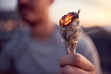 Man, hand and burning sage for a spiritual meditation on the beach at sunset for health and...
