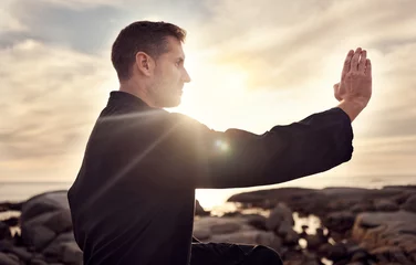 Fotobehang Karate man, martial arts and tai chi training to fight at beach against cloudy sunset sky for focus, power and energy outdoor. Male fighter ready for sports, fighting and exercise for fitness at sea © Beaunitta V W/peopleimages.com