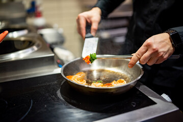 man chef cooking tasty shrimp in frying pan on kitchen