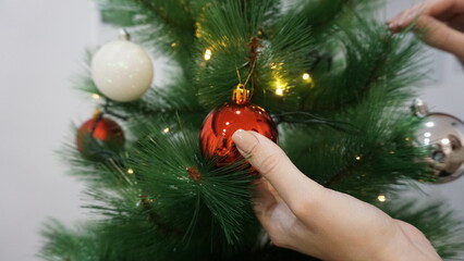 Decoración Navideña. Manos decorando el árbol de Navidad con bolas blancas y rojas.