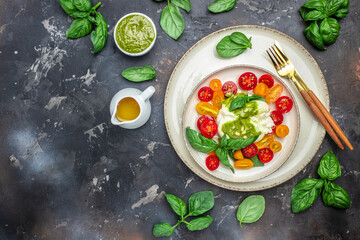 Salad with burrata cheese, cherry tomatoes and green pesto on a dark background. Restaurant menu, dieting, cookbook recipe top view