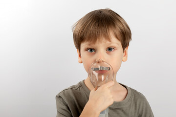 The boy breathes into the nebulizer on a light background