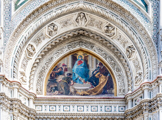 Close up on the façade of the Santa Maria del Fiore church or Florence Cathedral in neo-gothic style with white, green and red marbles, bas reliefs and frescoed lunette. 