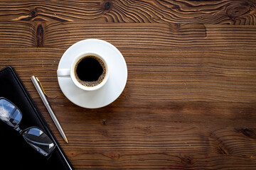 Office table with cup of hot black coffee and notebook