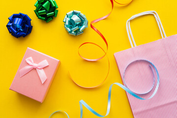 Top view of gift bows near present and shopping bag on yellow background.