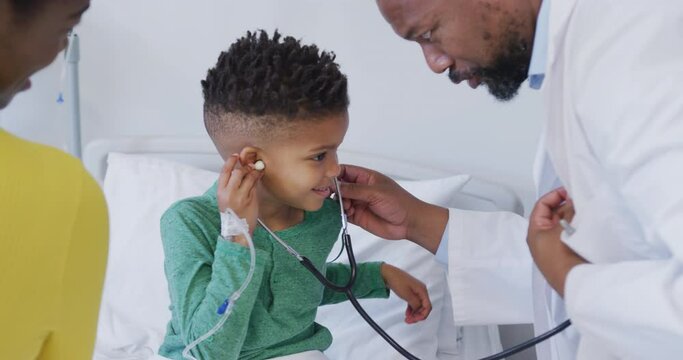 African american male doctor examining child patient, using stethoscope at hospital