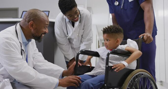 Diverse doctors talking to child patient sitting in wheelchair at hospital