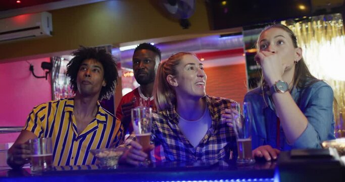 Video of diverse group of friends reacting to sports game on screen at a bar