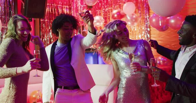 Video of a diverse group of happy friends dancing with glasses of champagne at a nightclub