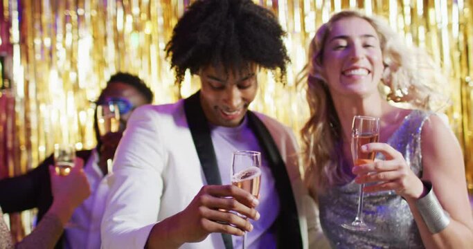 Video of happy diverse couple dancing holding glasses of champagne at a nightclub