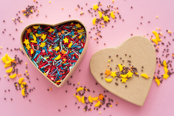 Top view of sweet sprinkles in gift box in heart shape on pink background.