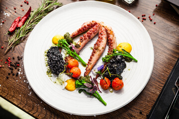 Octopus with black risotto. Carrot cream, mini-broccoli, basil pesto. Delicious healthy traditional food closeup served for lunch in modern gourmet cuisine restaurant